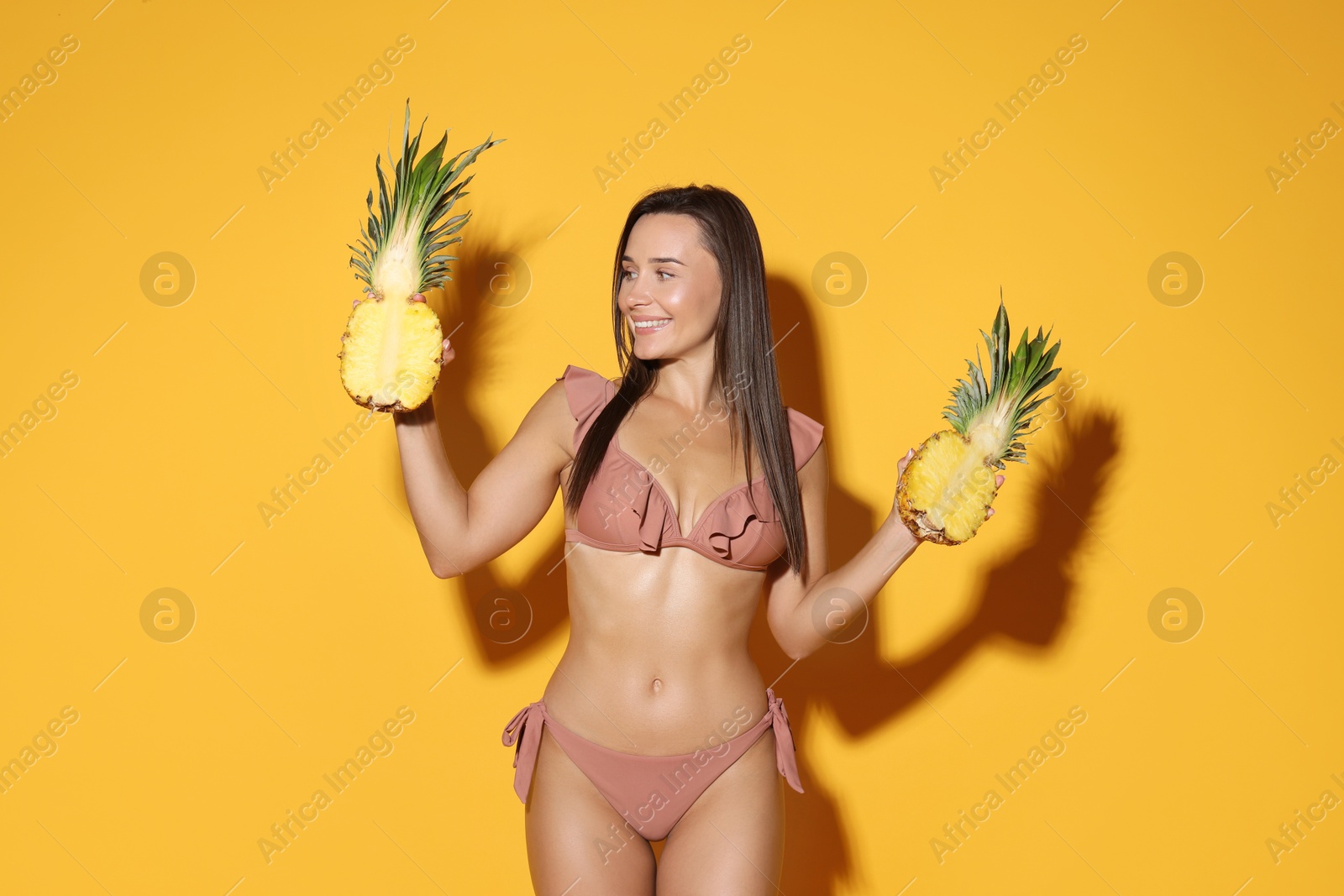 Photo of Attractive woman in bikini with halves of pineapple on orange background