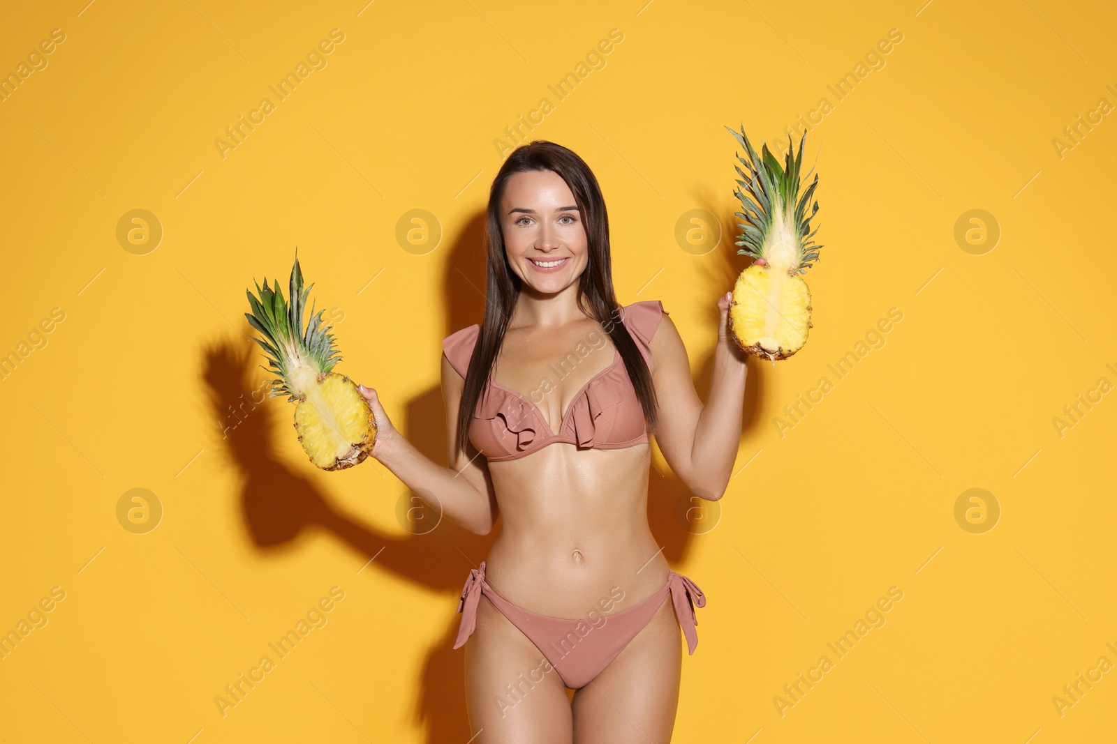 Photo of Attractive woman in bikini with halves of pineapple on orange background