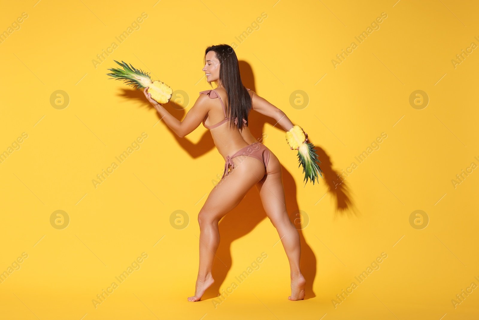 Photo of Woman in bikini with halves of pineapple on orange background