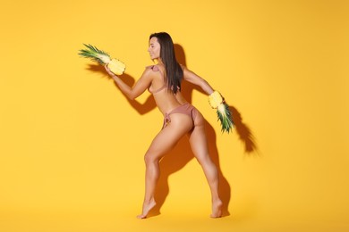 Woman in bikini with halves of pineapple on orange background