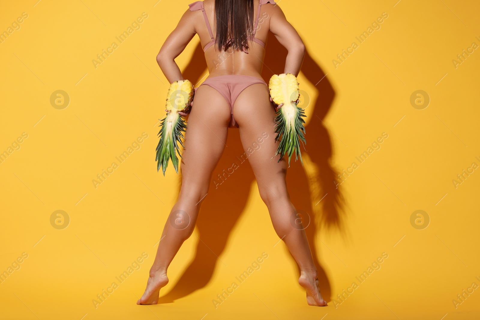 Photo of Woman in bikini with halves of pineapple on orange background, closeup