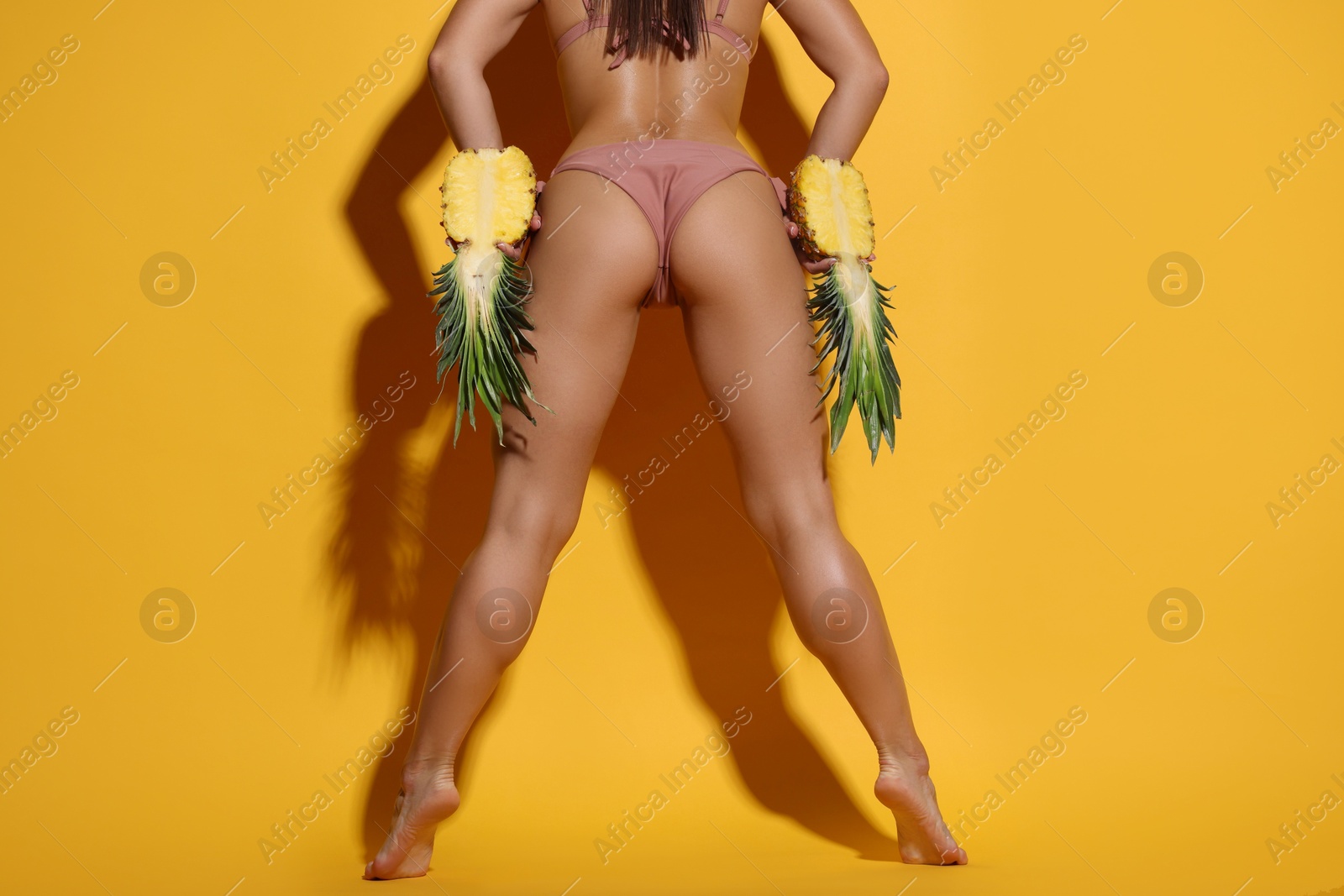 Photo of Woman in bikini with halves of pineapple on orange background, closeup