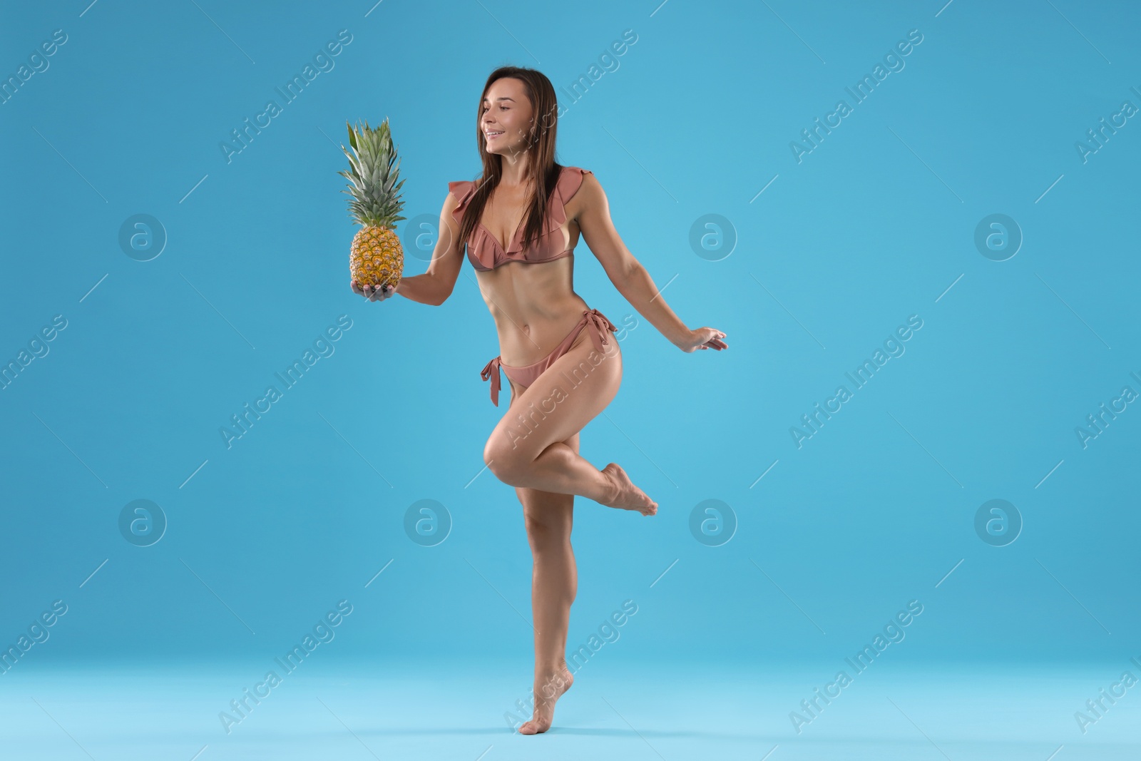 Photo of Woman in bikini with fresh pineapple on light blue background