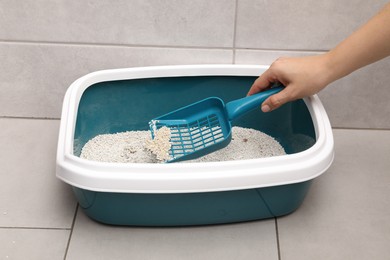 Woman cleaning cat litter tray with scoop indoors, closeup