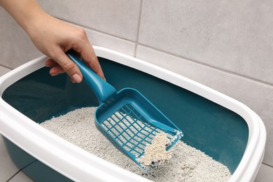 Photo of Woman cleaning cat litter tray with scoop indoors, closeup