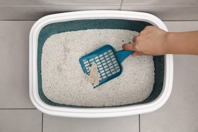 Photo of Woman cleaning cat litter tray with scoop indoors, top view