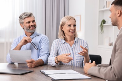 Pension plan. Couple consulting with insurance agent at table indoors