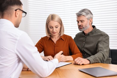 Pension plan. Couple consulting with insurance agent at table indoors