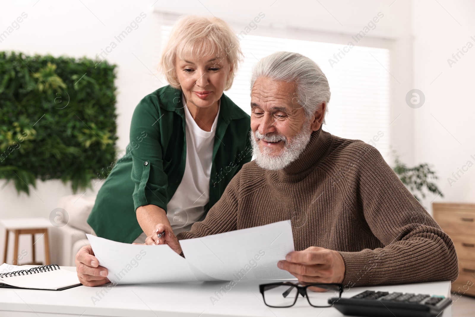 Photo of Pension savings. Senior couple planning budget at white table indoors