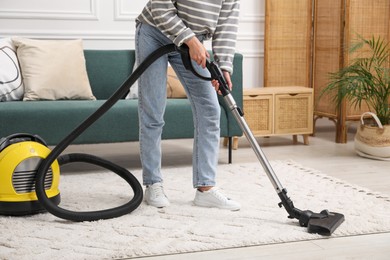 Photo of Woman cleaning carpet with vacuum in living room, closeup