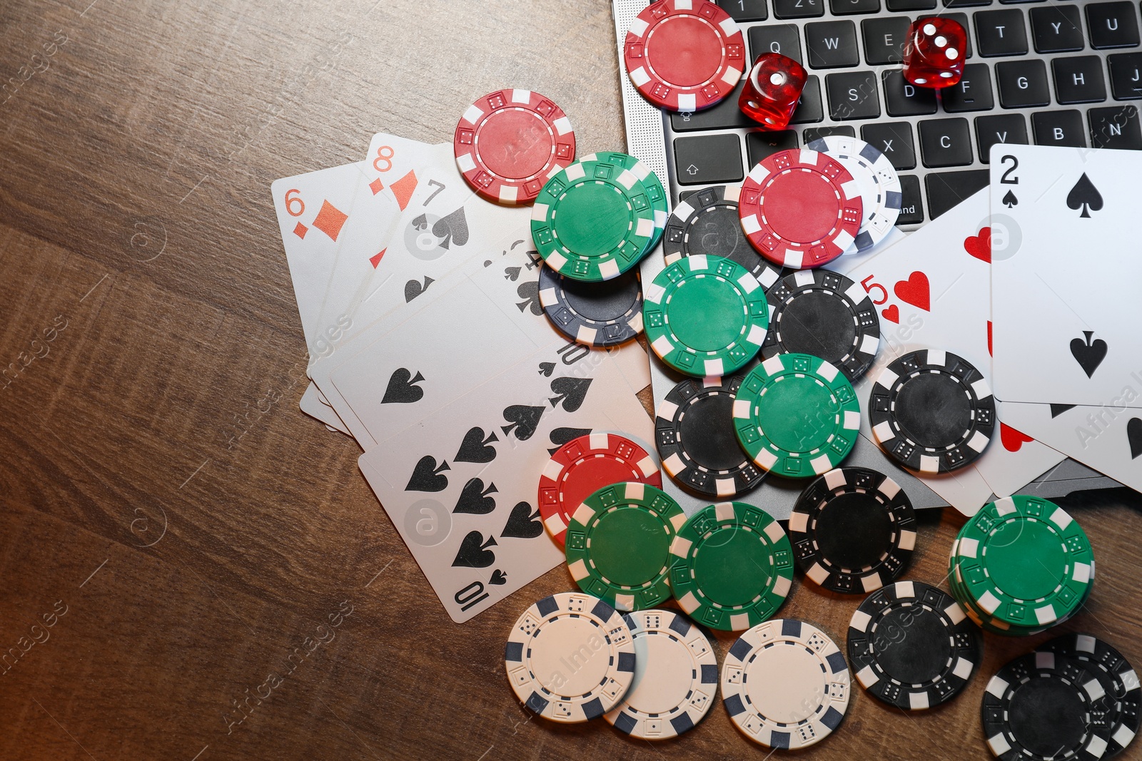 Photo of Poker chips, laptop, playing cards and dices on wooden table, flat lay. Online game