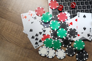 Poker chips, laptop, playing cards and dices on wooden table, flat lay. Online game