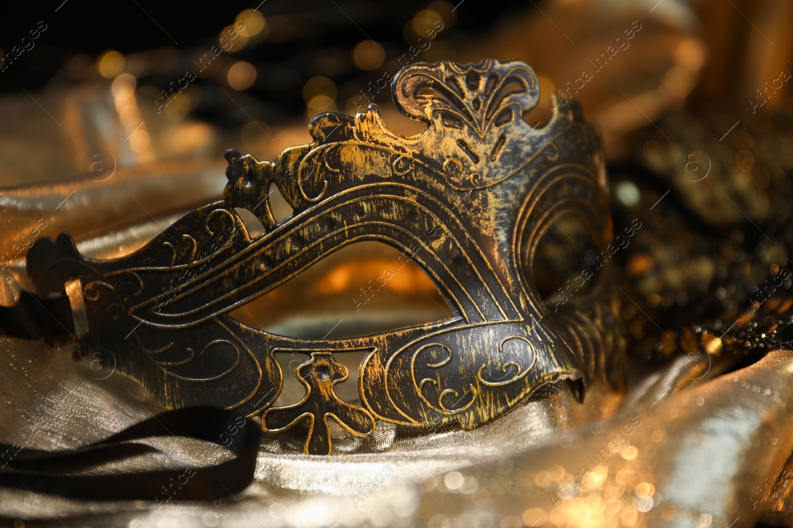 Photo of Beautiful carnival mask on golden fabric, closeup