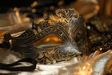 Photo of Beautiful carnival mask on golden fabric, closeup