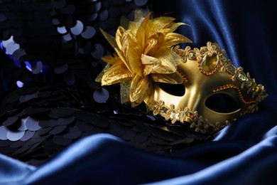 Photo of Beautiful golden carnival mask on blue fabric in darkness