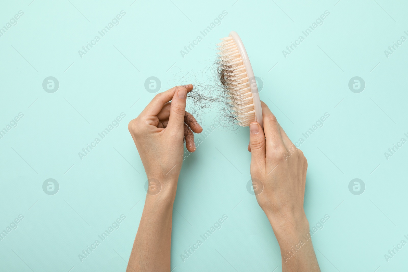 Photo of Woman taking her lost hair from brush on light blue background, top view. Alopecia problem