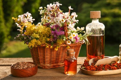 Photo of Tincture in bottles, different flowers and bark chips on wooden table outdoors