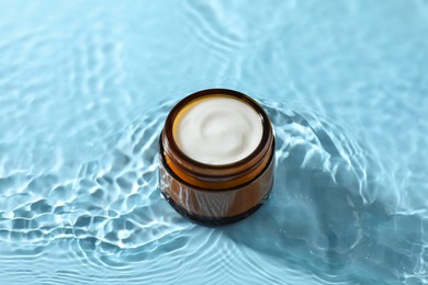 Photo of Jar with face cream in water on light blue background