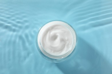 Photo of Jar with face cream in water on light blue background, top view