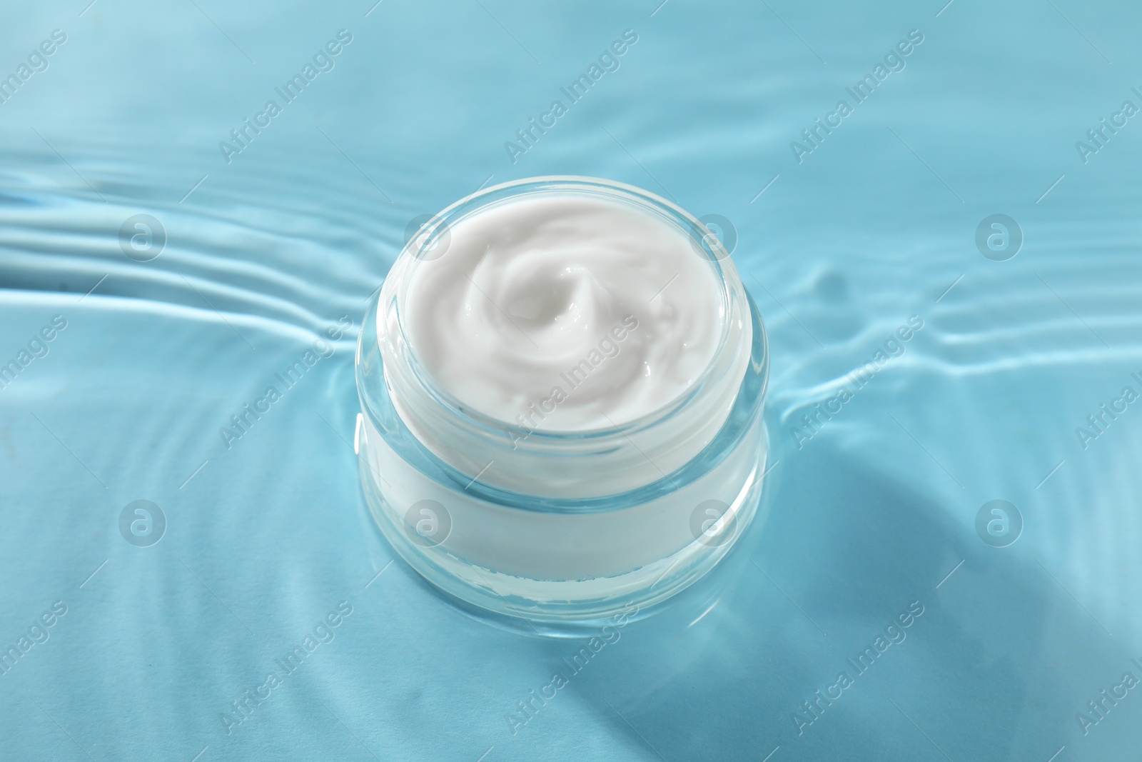 Photo of Jar with face cream in water on light blue background