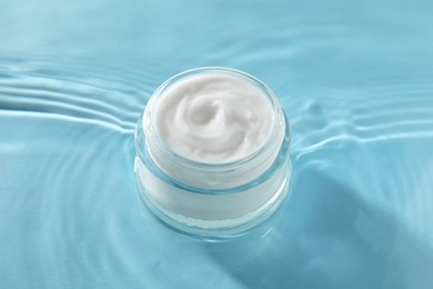 Jar with face cream in water on light blue background