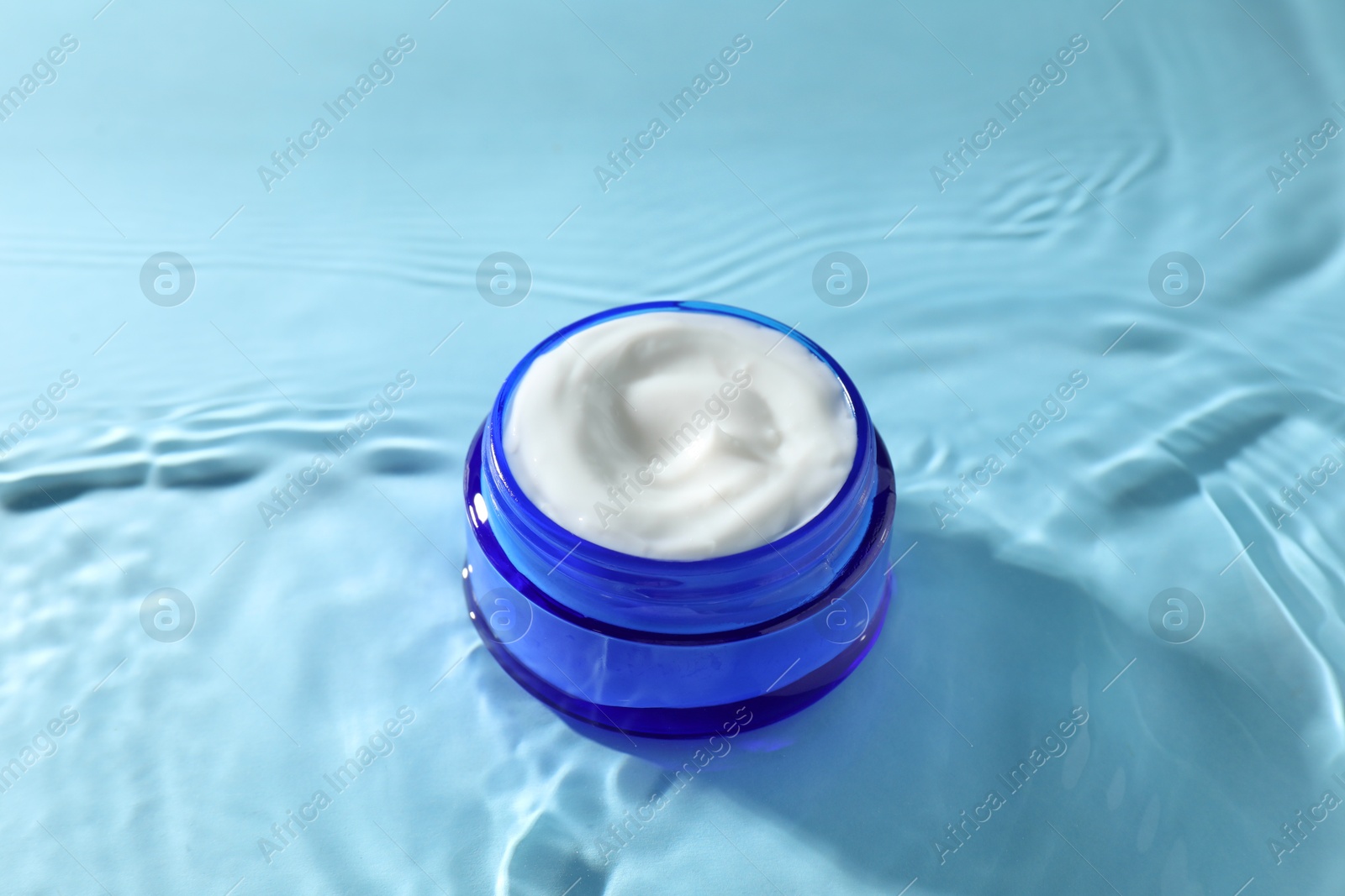 Photo of Jar with face cream in water on light blue background