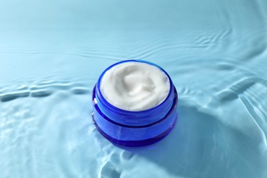 Photo of Jar with face cream in water on light blue background