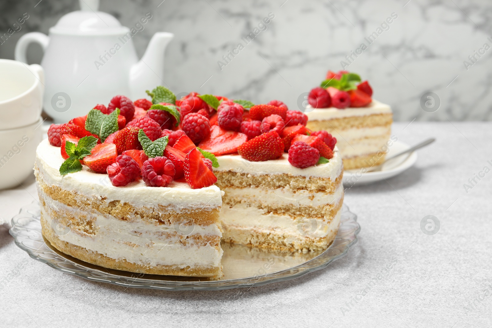 Photo of Tasty sponge cake with fresh berries and mint on light gray table, closeup