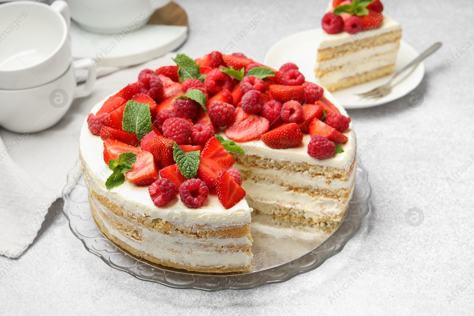 Photo of Tasty sponge cake with fresh berries and mint on light gray table, closeup