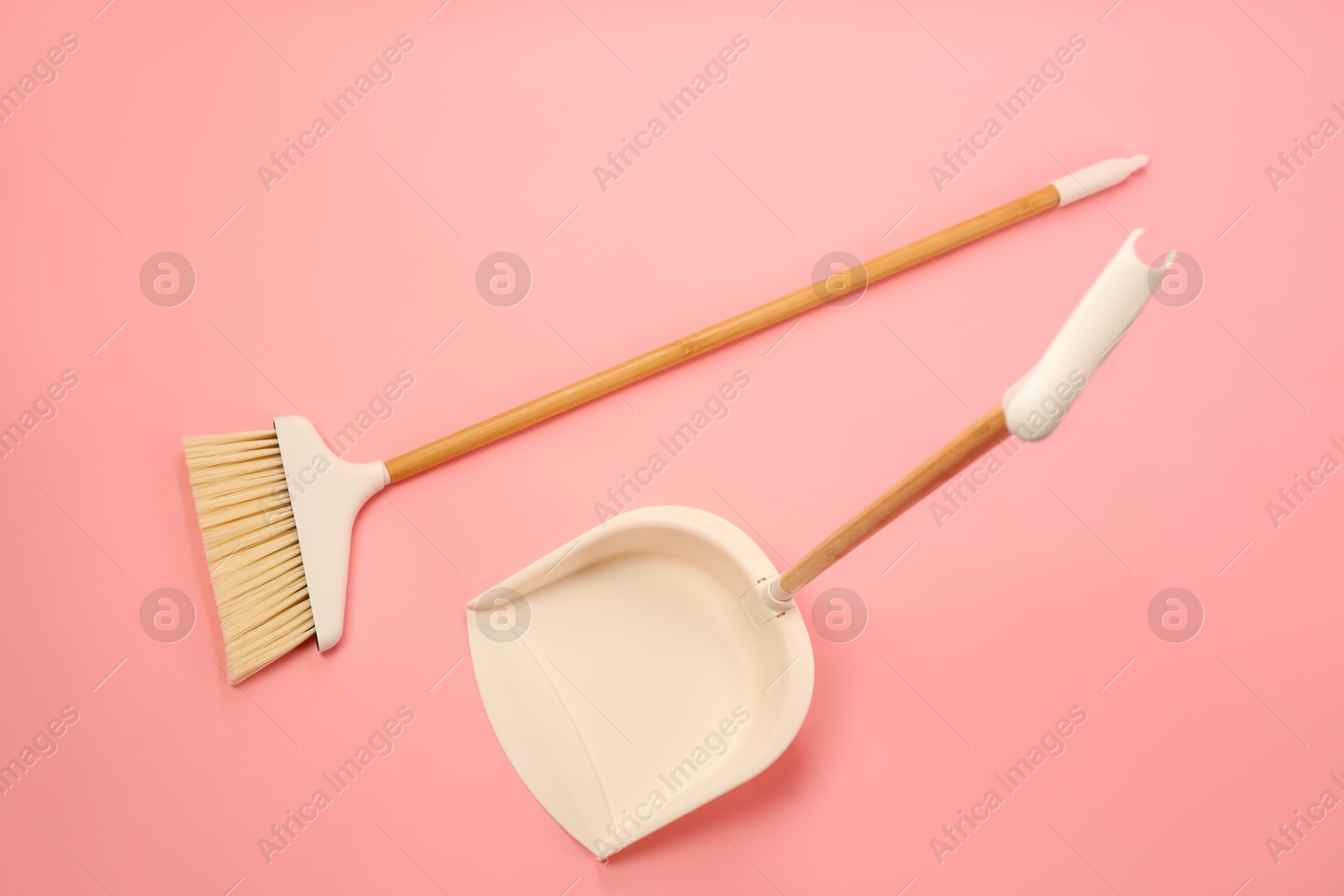 Photo of Cleaning broom and dustpan on pink background, flat lay