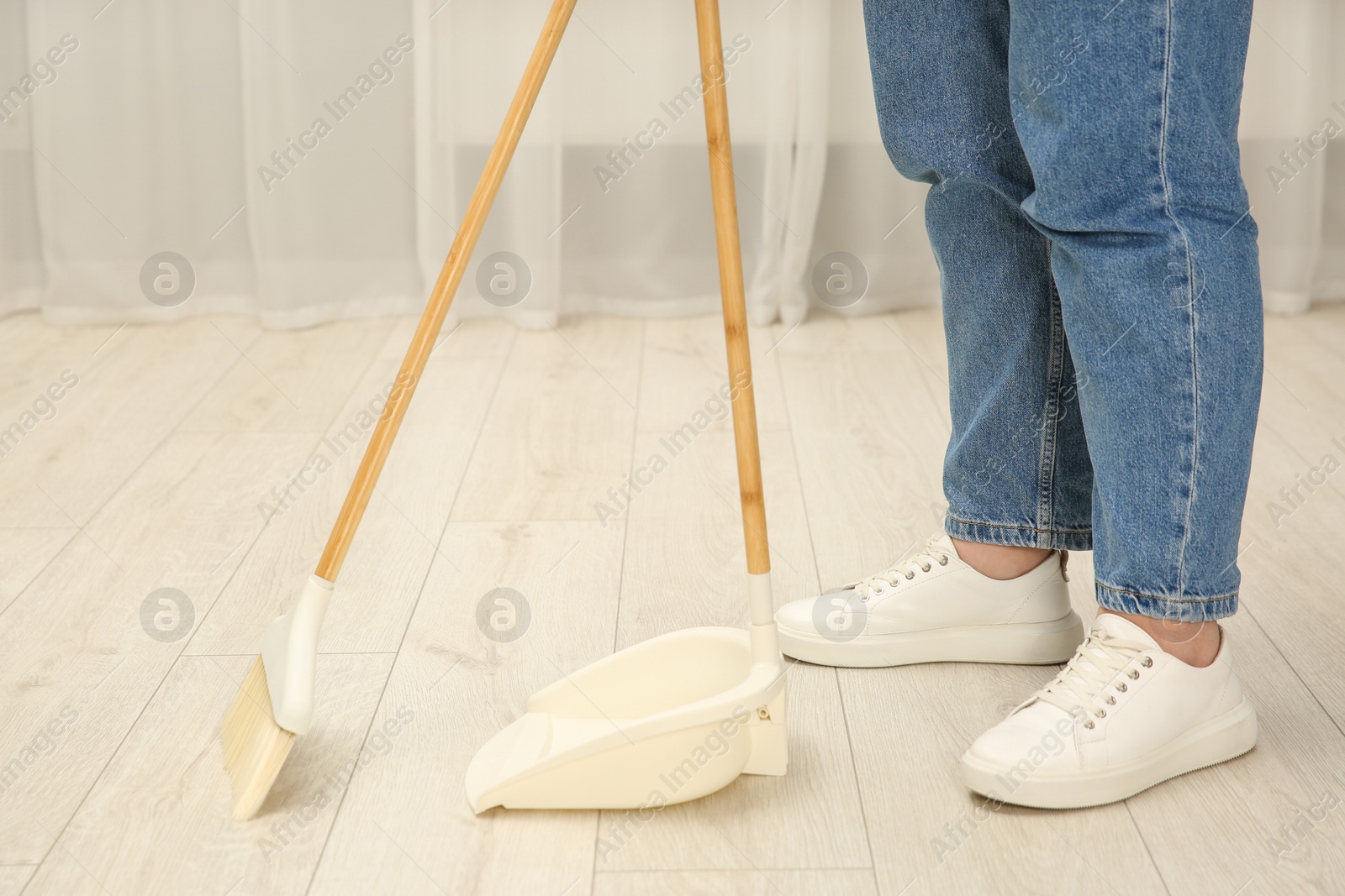 Photo of Woman with broom and dustpan cleaning floor indoors, closeup