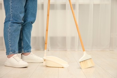 Photo of Woman with broom and dustpan cleaning floor indoors, closeup