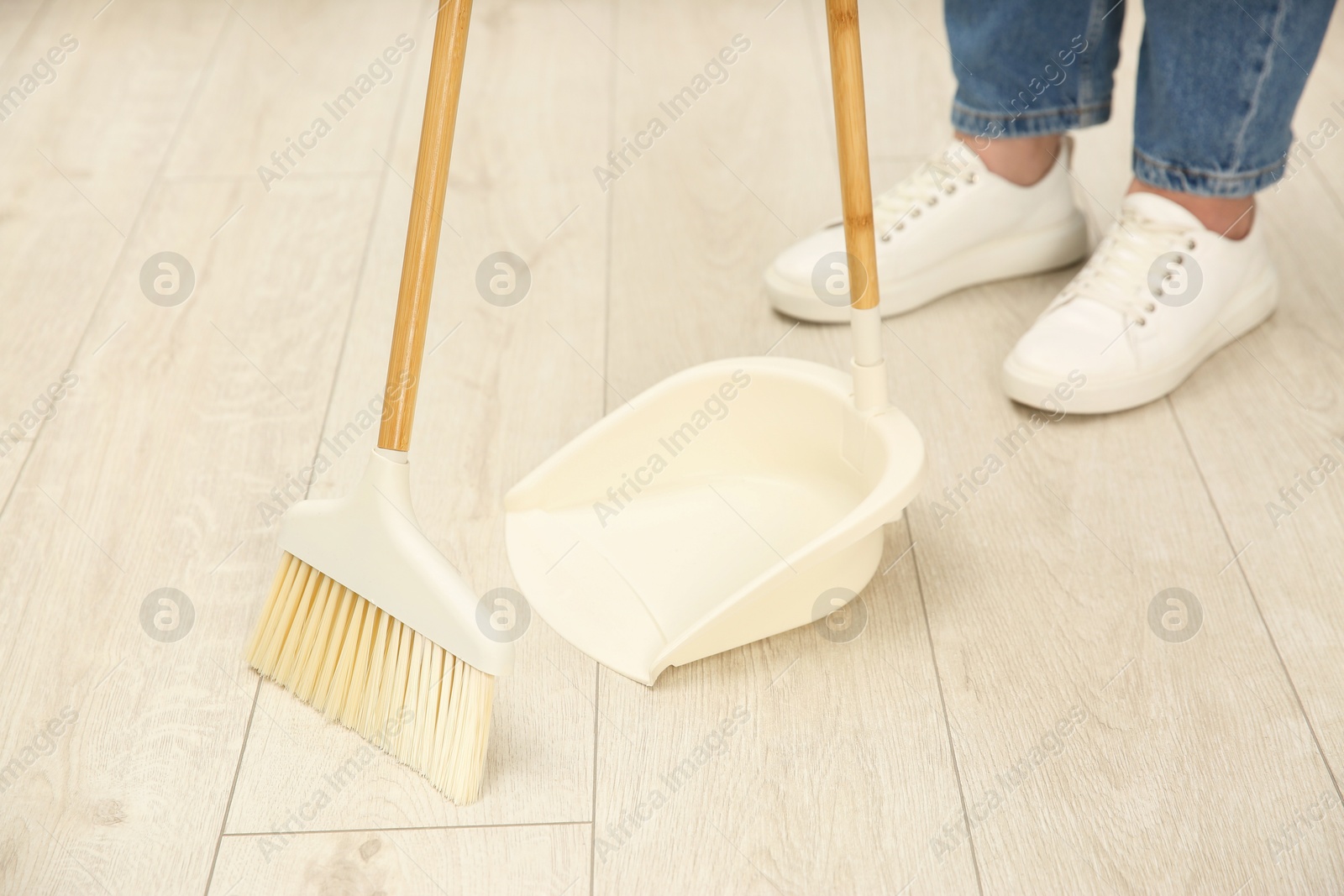 Photo of Woman with broom and dustpan cleaning floor indoors, closeup