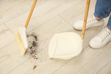 Photo of Woman with broom and dustpan cleaning floor indoors, closeup