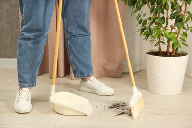 Photo of Woman with broom and dustpan cleaning floor indoors, closeup