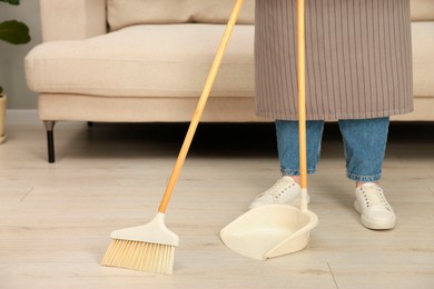 Woman with broom and dustpan cleaning floor indoors, closeup