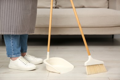 Photo of Woman with broom and dustpan cleaning floor indoors, closeup