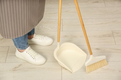 Photo of Woman with broom and dustpan cleaning floor indoors, closeup