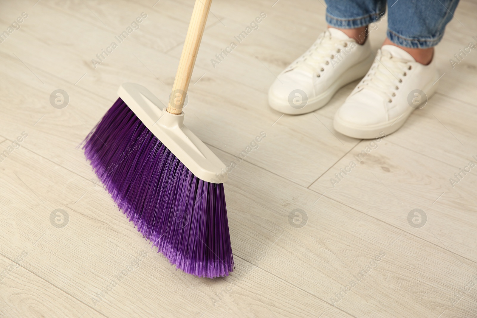 Photo of Woman with broom sweeping floor indoors, closeup