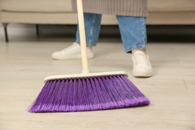 Photo of Woman with broom sweeping floor indoors, closeup