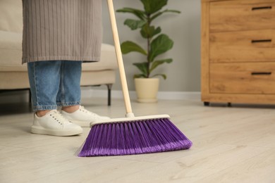 Photo of Woman with broom sweeping floor indoors, closeup