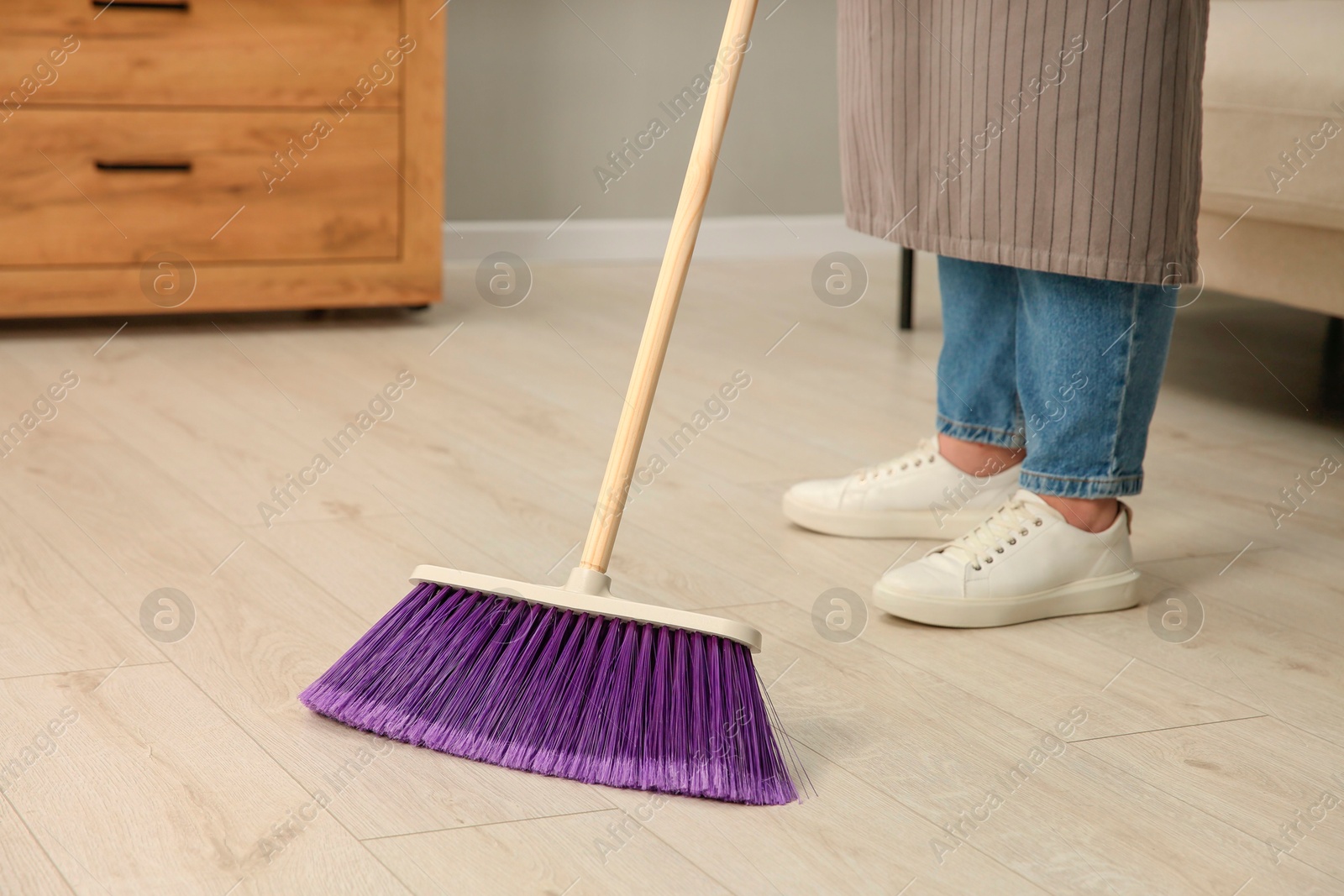 Photo of Woman with broom sweeping floor indoors, closeup