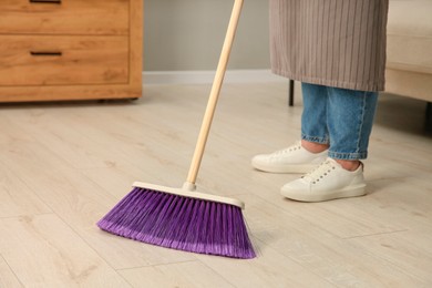 Photo of Woman with broom sweeping floor indoors, closeup