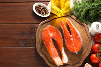 Photo of Board with fresh salmon steaks, spices and products on wooden table, flat lay. Space for text