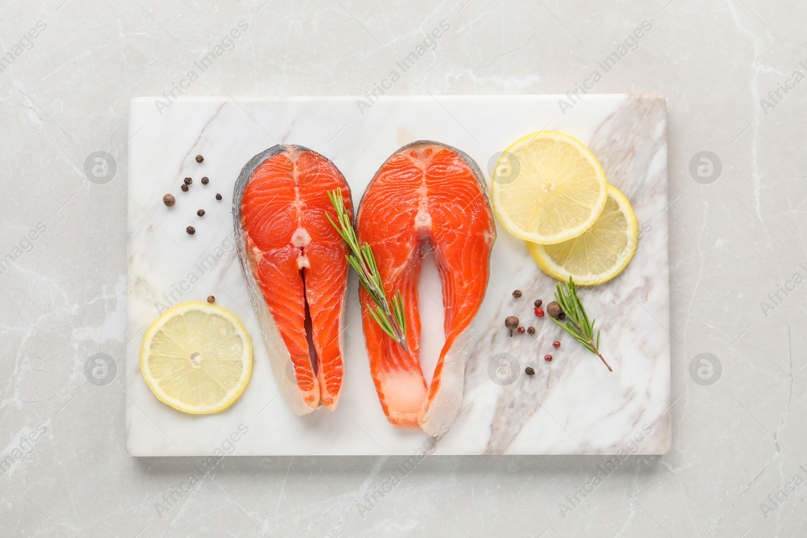 Photo of Board with fresh salmon steaks, peppercorns, rosemary and lemon on light marble table, top view