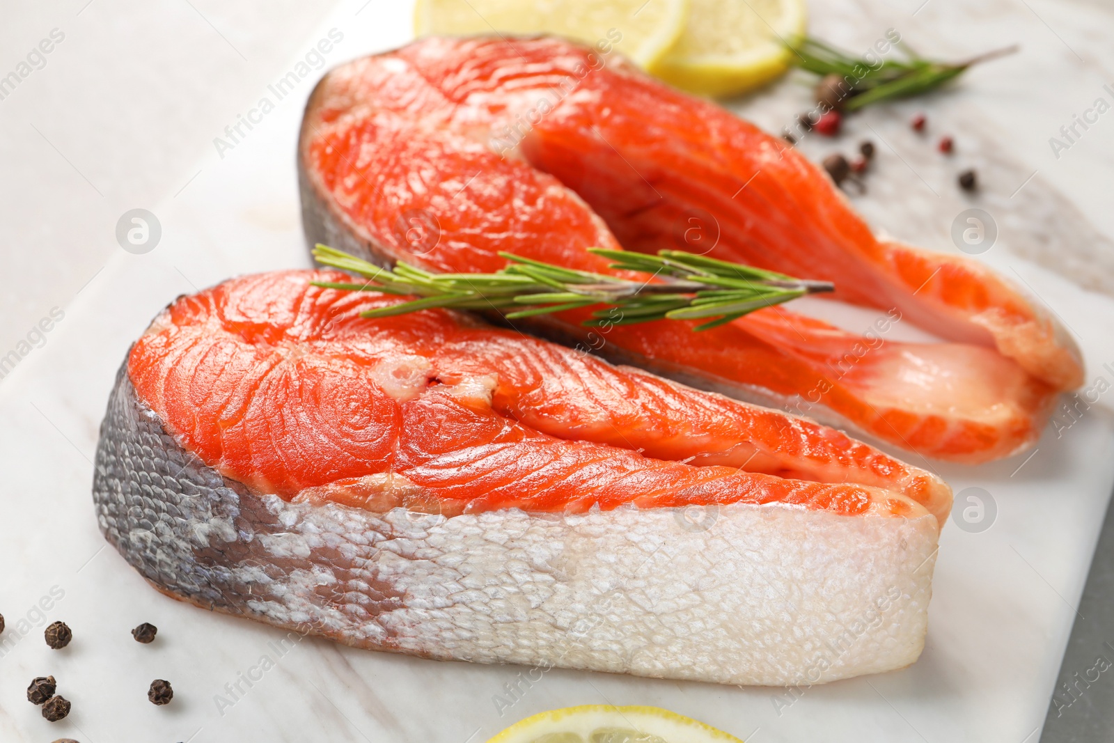 Photo of Board with fresh salmon steaks, peppercorns and rosemary on light table, closeup