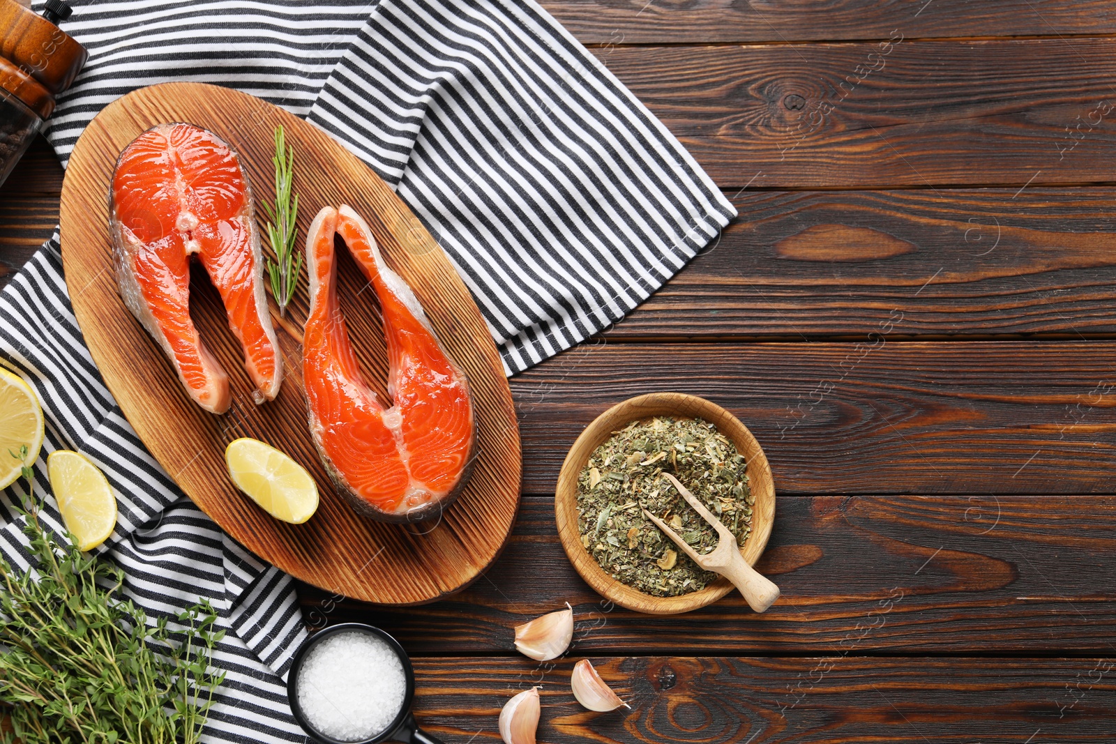 Photo of Board with fresh salmon steaks, spices, herbs and lemon on wooden table, flat lay. Space for text