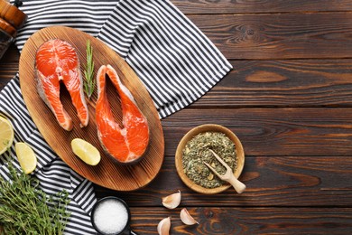 Photo of Board with fresh salmon steaks, spices, herbs and lemon on wooden table, flat lay. Space for text