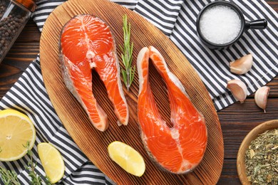 Photo of Board with fresh salmon steaks, spices, rosemary and lemon on wooden table, flat lay