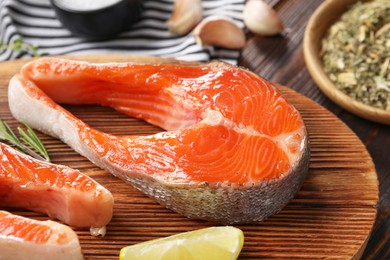 Photo of Board with fresh salmon steaks and lemon on wooden table, closeup